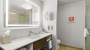 A modern bathroom with a large mirror, two sinks, a glass shower enclosure, and a toilet.