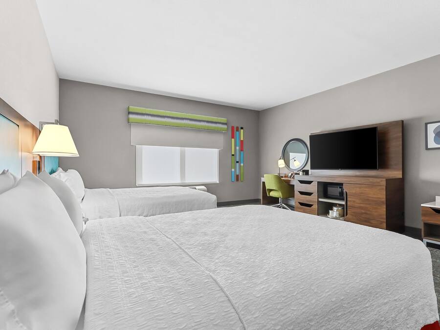 A hotel room with two beds, a TV, a desk, a lamp, and a mirror.