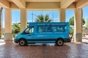 A blue delivery van parked under a covered area with palm trees and a clear sky in the background. - Hampton Inn & Suites El Paso West (El Paso)
