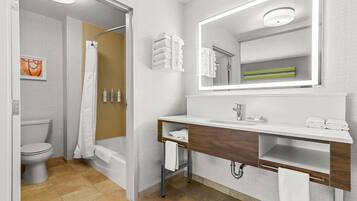 A modern bathroom with a toilet, shower, and sink, featuring a mirror, towel rack, and a framed picture on the wall.
