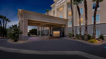 A hotel entrance with a covered walkway, palm trees, and a clear sky.