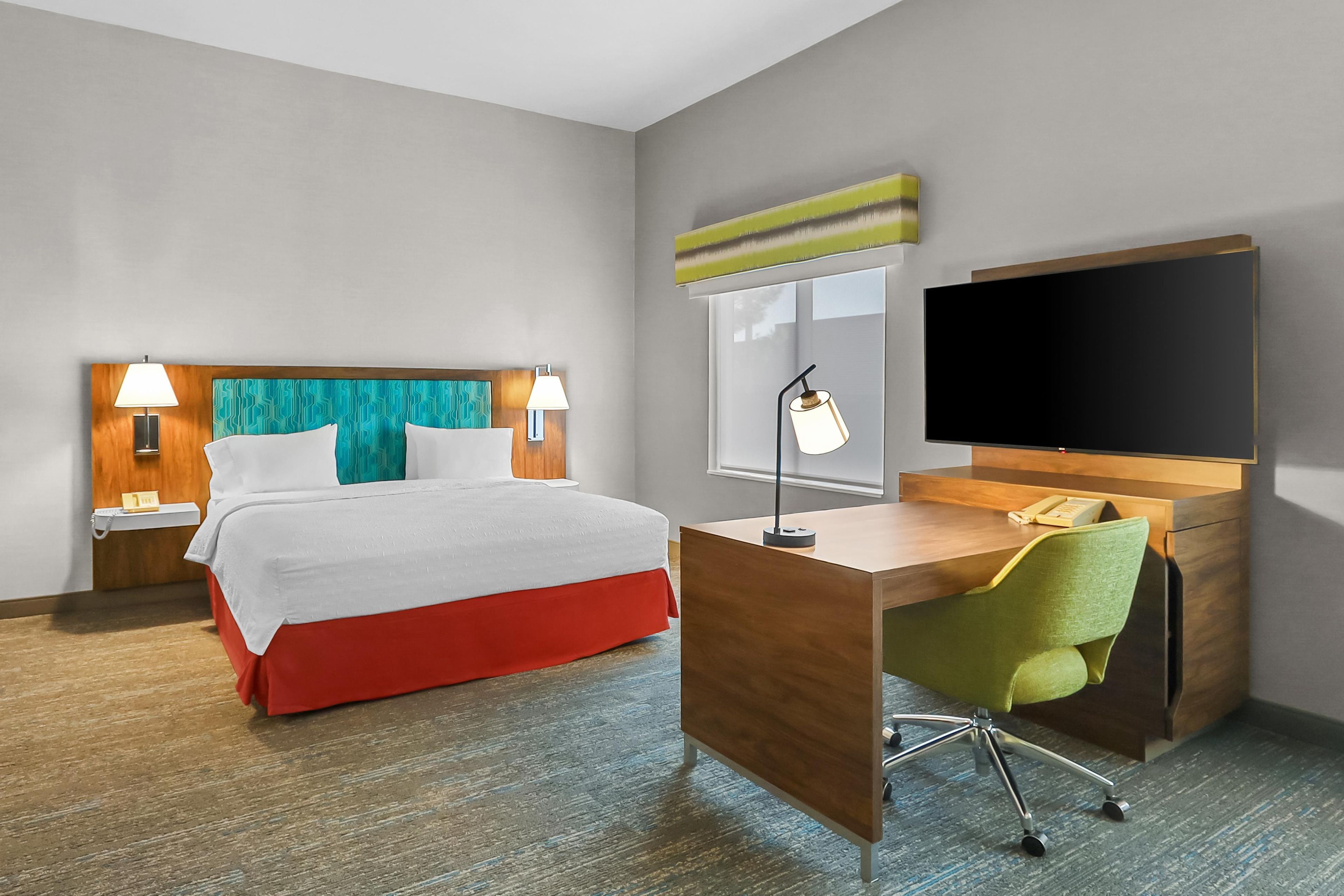 A hotel room with a bed, desk, chair, TV, and bedside lamps.