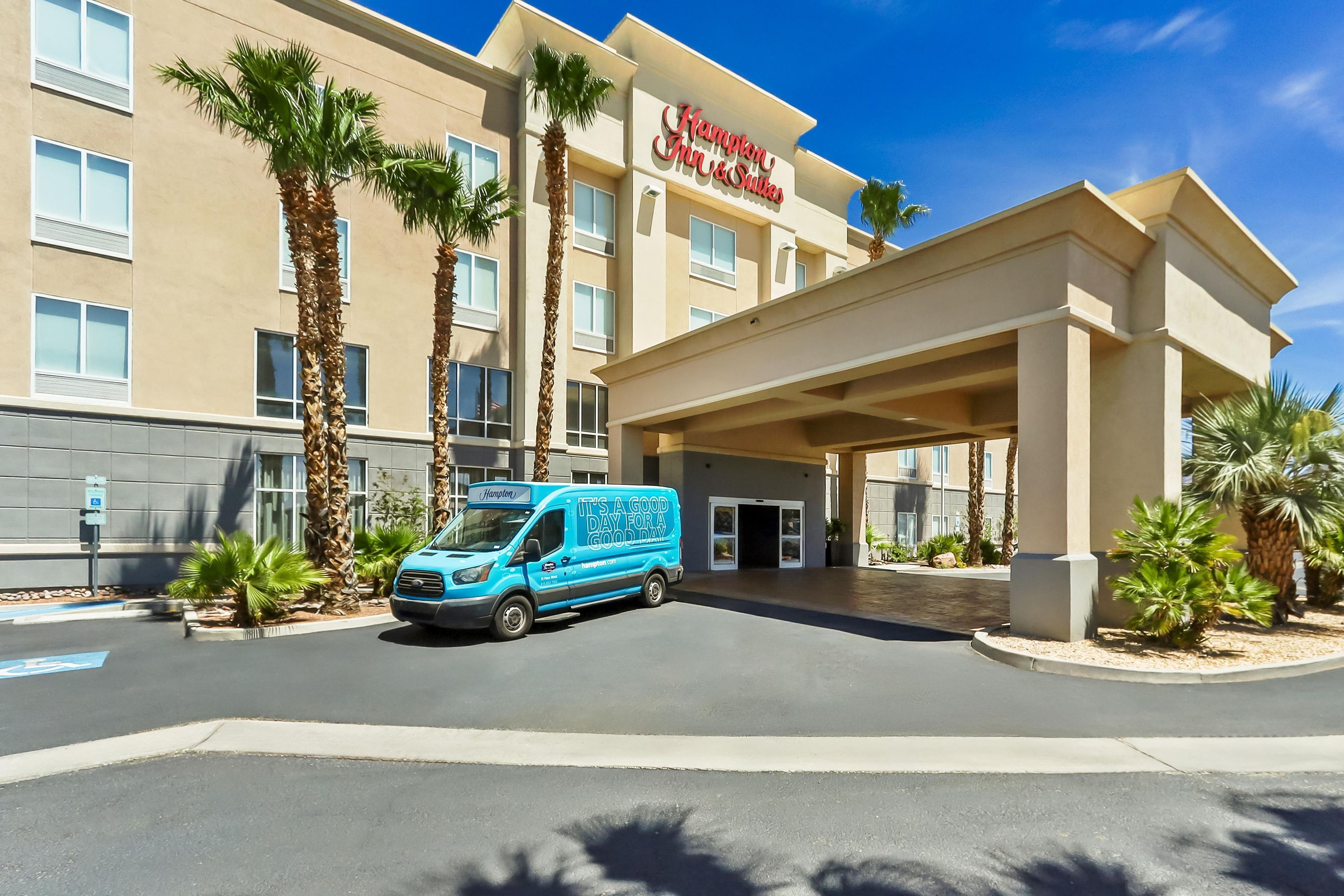 A Hampton Inn & Suites hotel with a blue van in front, palm trees, and a clear blue sky.