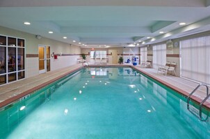 Una piscina interior con agua cristalina, rodeada de sillones de descanso y una pared de azulejos.