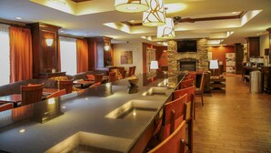 A spacious bar area with a long counter, multiple seating options, and a stone fireplace. - Hampton Inn Matamoras/Milford (Matamoras)