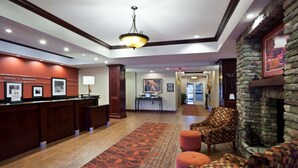 A hotel lobby with a reception desk, a patterned carpet, a stone wall, and a seating area with a checkered sofa and ottoman. - Hampton Inn Matamoras/Milford (Matamoras)