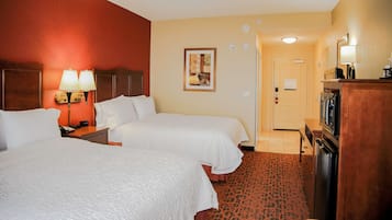 Een hotelkamer met twee bedden, een bureau, een televisie en een deur naar een badkamer.