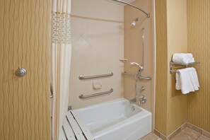 A modern bathroom with a bathtub, grab bars, a showerhead, and a towel rack.
