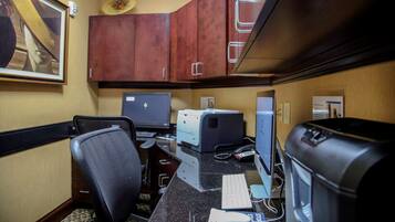 Una oficina de hotel con escritorio, computadora, impresora y una silla.