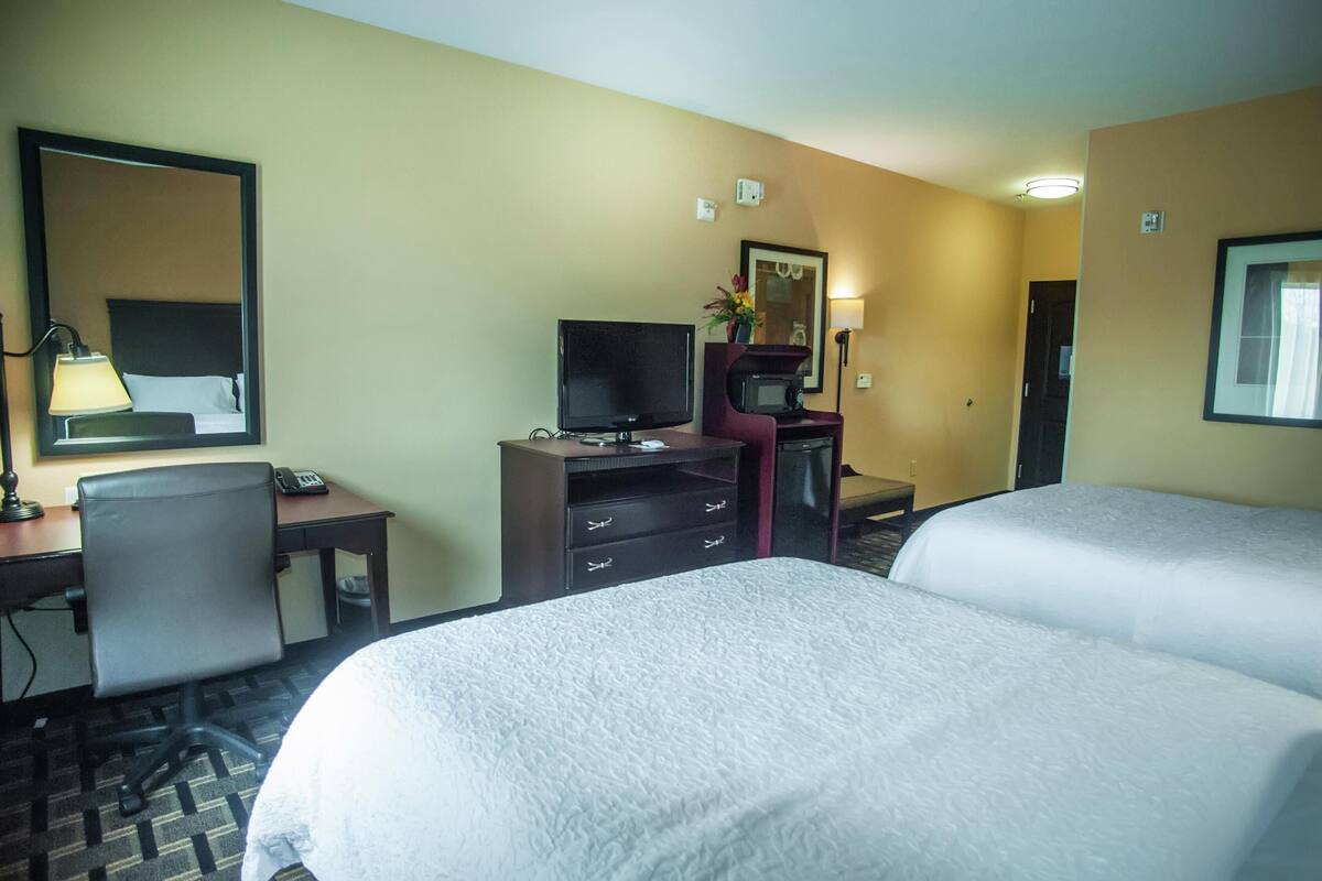 A hotel room with two beds, a desk with a computer, a television, a microwave, and a telephone.