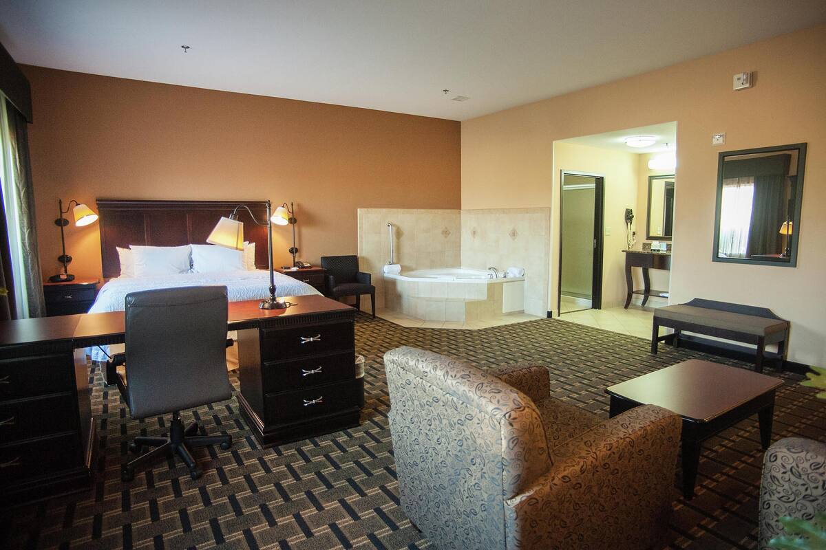 A hotel room with a bed, desk, chair, sofa, and a bathroom with a bathtub.