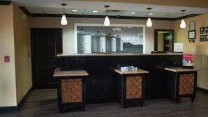A reception area with a counter, two stools, hanging pendant lights, and a backdrop with the word "explore". - Hampton Inn & Suites Palestine (Palestine)