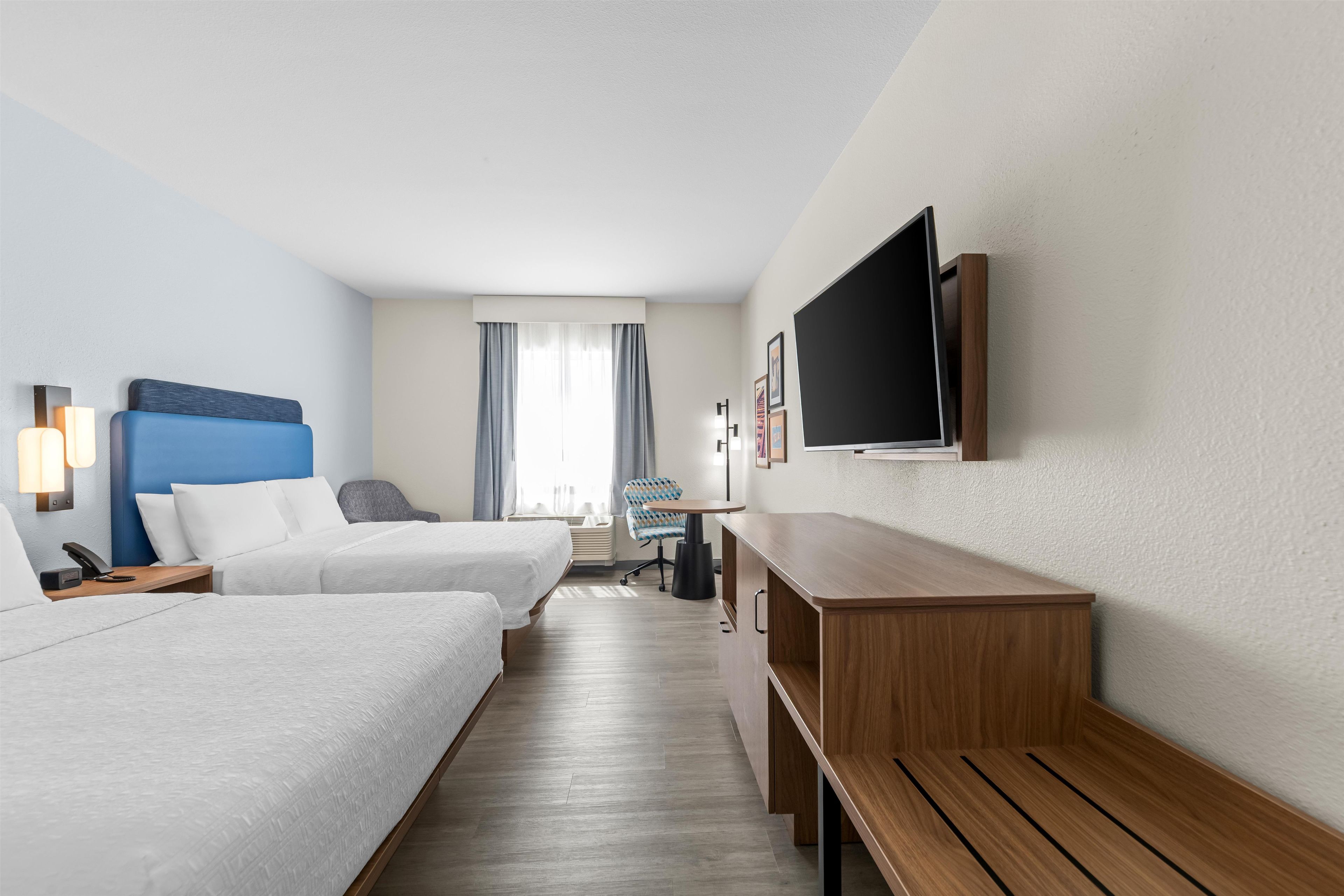 Habitación de hotel con dos camas, un escritorio, una silla, un televisor y una ventana con cortinas.