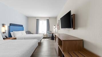 Habitación de hotel con dos camas, un escritorio, una silla, un televisor y una ventana con cortinas.