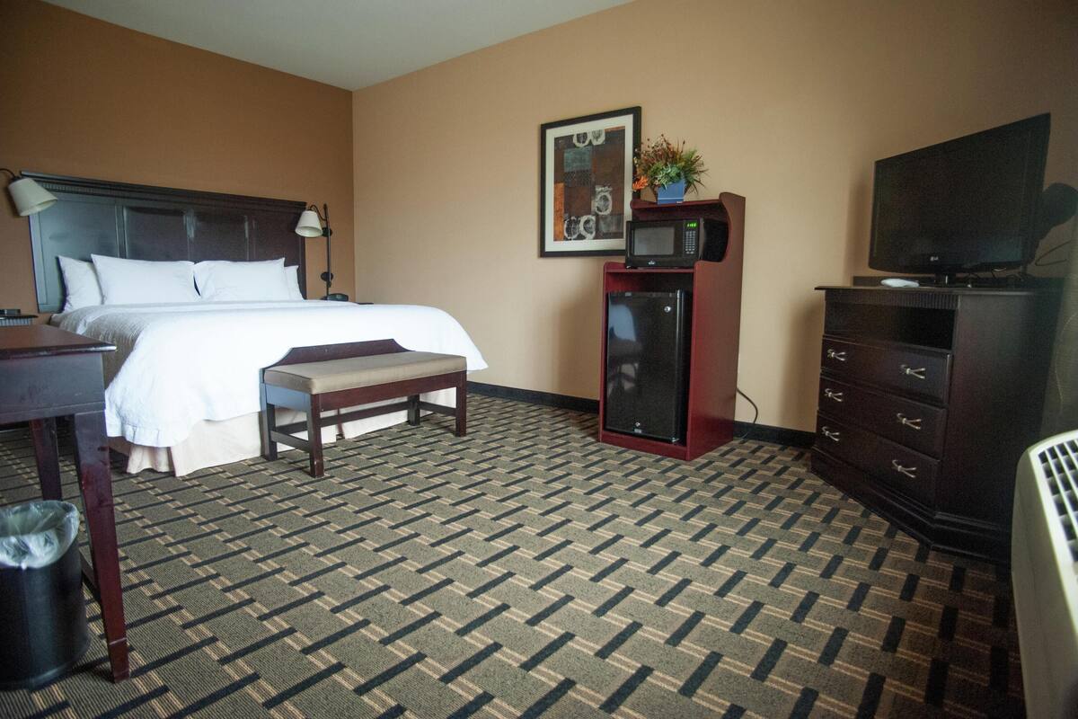 A hotel room with a bed, a desk, a chair, a microwave, a television, and a dresser.