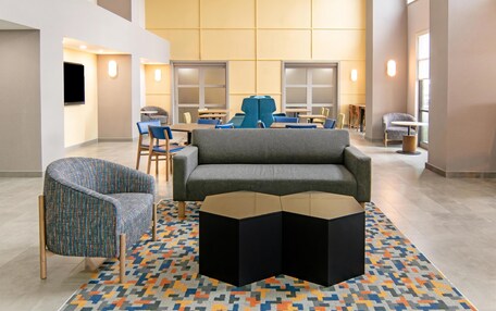 A modern hotel lobby with a grey sofa, patterned armchair, and a central coffee table.
