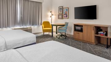 A hotel room with two beds, a desk, a TV, and a minibar.
