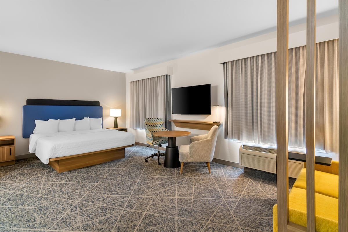 A hotel room with a bed, a desk, a chair, a TV, and a window with curtains.