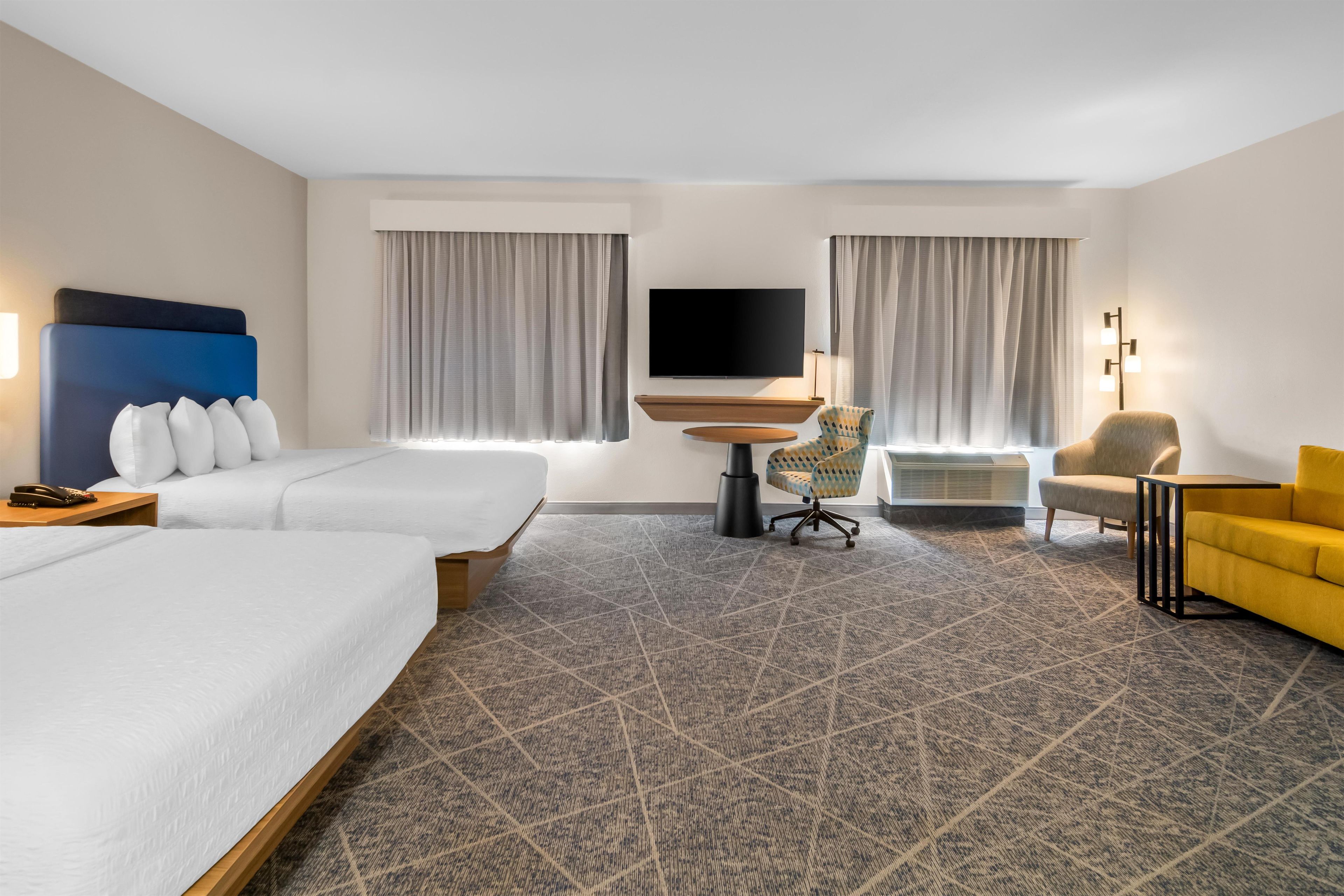 A hotel room with a large bed, a desk, a chair, a TV, and a sofa.
