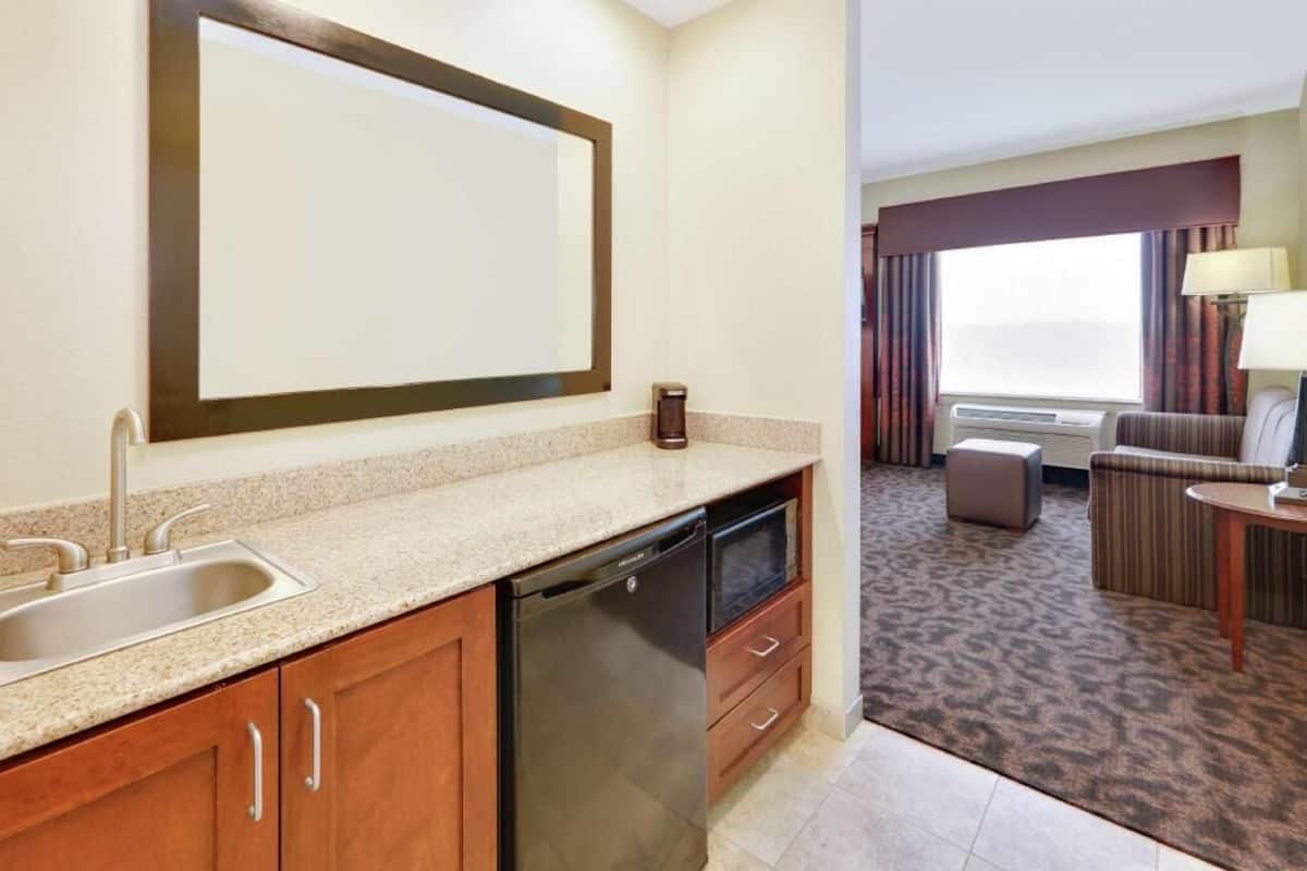 A hotel room with a kitchenette, a sink, a dishwasher, a sofa, a table, and a large window.