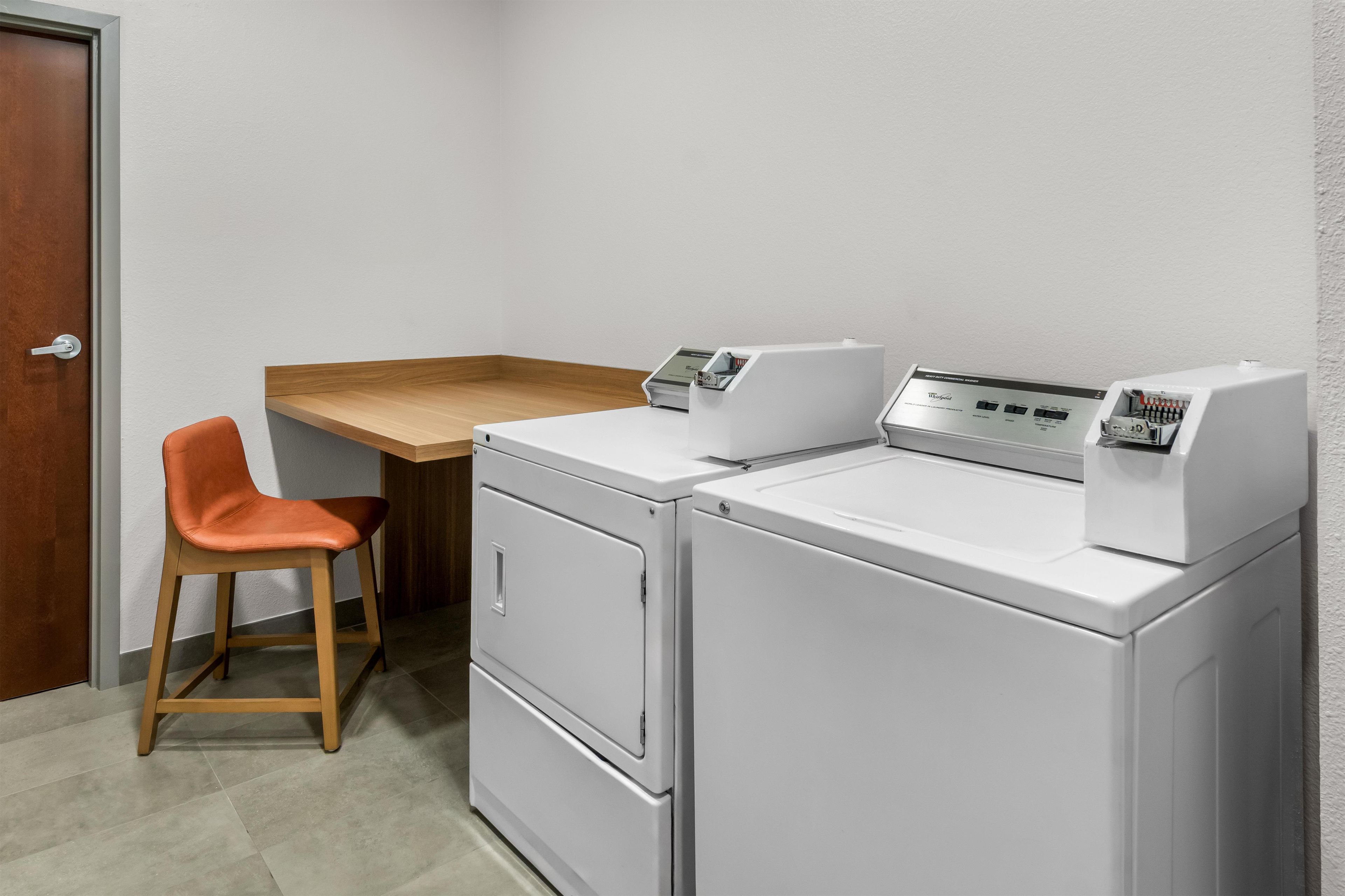 A laundry room with a washing machine, dryer, and a wooden table with a chair.