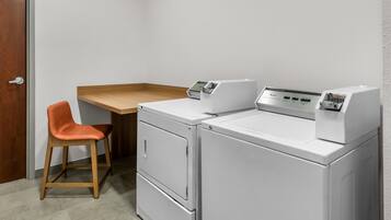A laundry room with a washing machine, dryer, and a wooden table with a chair.