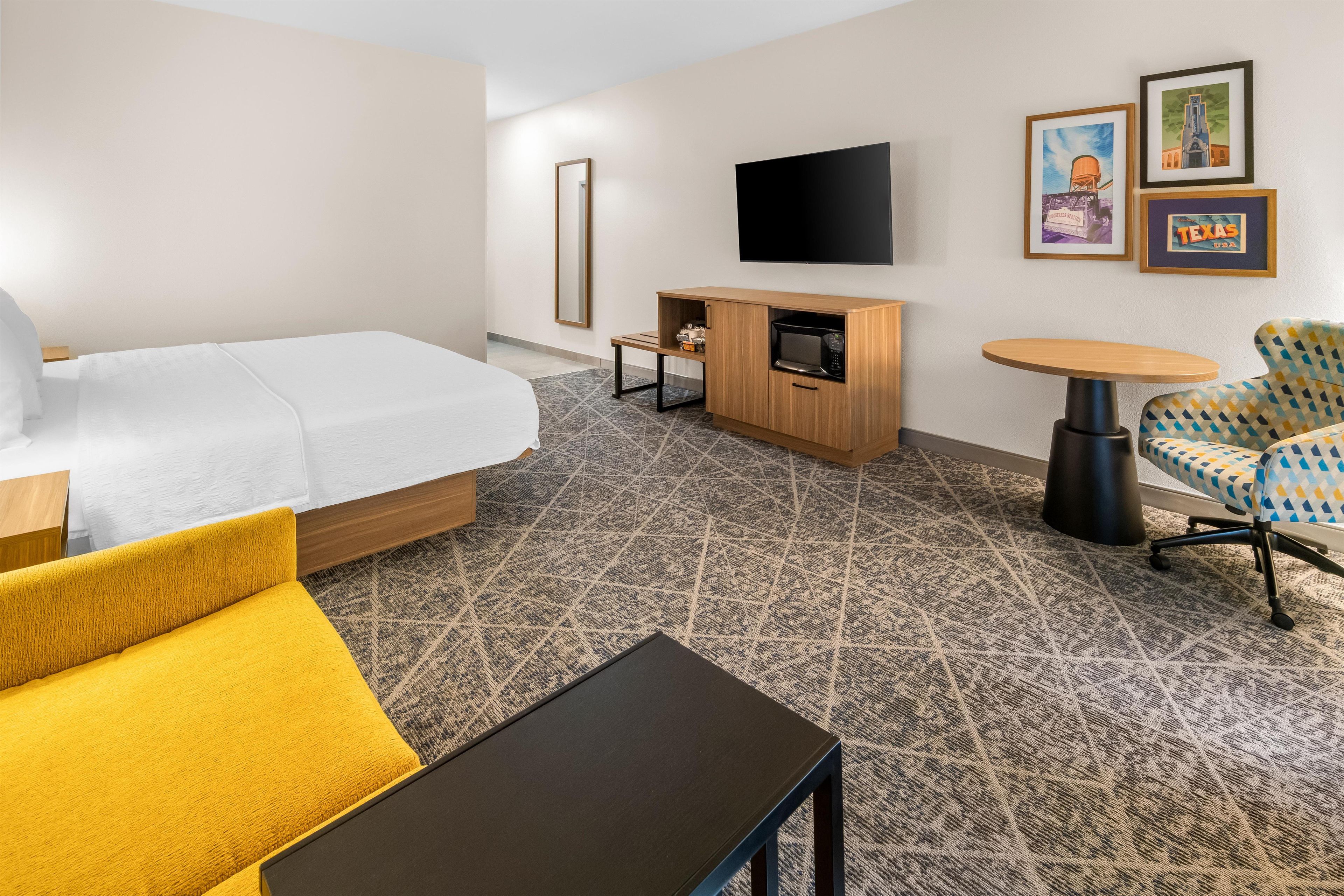 A hotel room with a bed, a sofa, a small table, a TV, and a microwave.