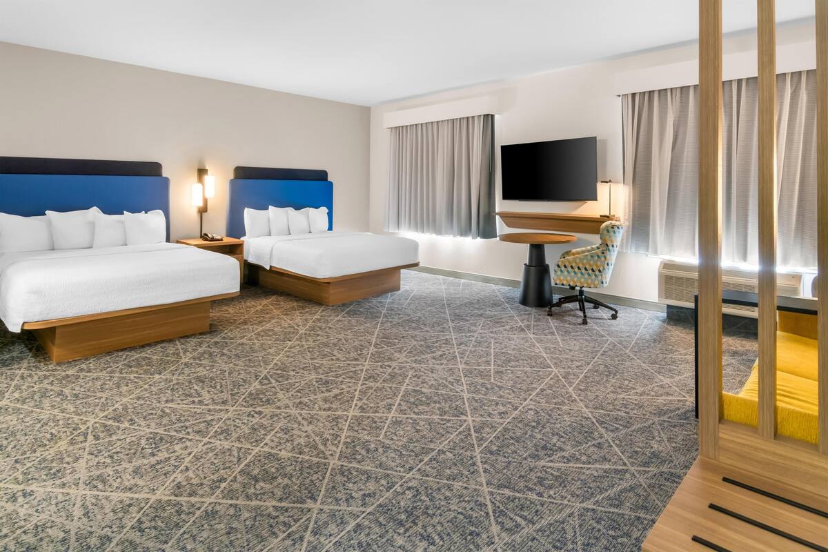A hotel room with two beds, a TV, a desk, and a chair.