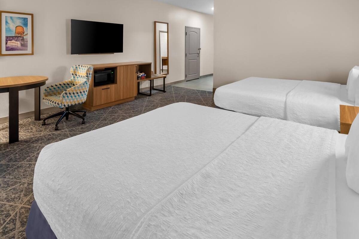 A hotel room with two beds, a desk with a chair, a television, a mirror, and a door.