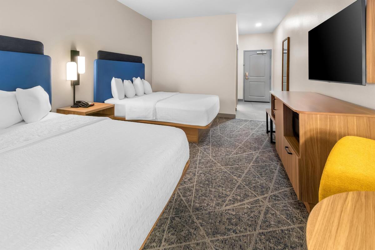A hotel room with two beds, a TV, a desk, and a chair.