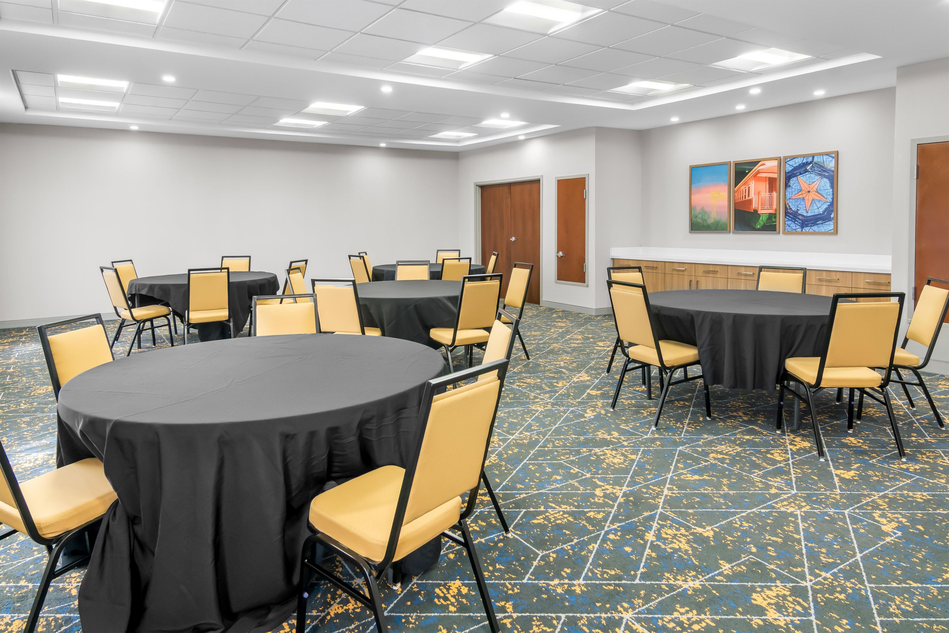 Uma sala de conferências com várias mesas e cadeiras, piso de azulejos e obras de arte nas paredes.