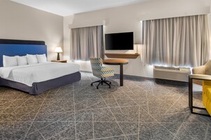 Habitación de hotel con cama, escritorio, silla, televisor de pantalla plana y ventana con cortinas.