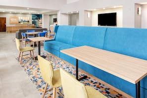 A modern hotel lobby with a blue sofa, wooden tables, and chairs. - Hampton Inn and Suites Fort Worth/Forest Hill (Fort Worth)