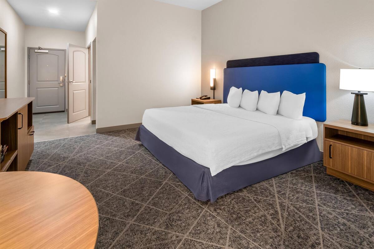 A hotel room with a bed, bedside table, lamp, and a desk with a chair.