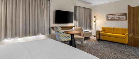 A hotel room with a bed, a desk, a chair, a sofa, and a television.