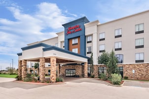 Un hotel Hampton Inn & Suites con entrada techada, fachada de ladrillo y varias ventanas.