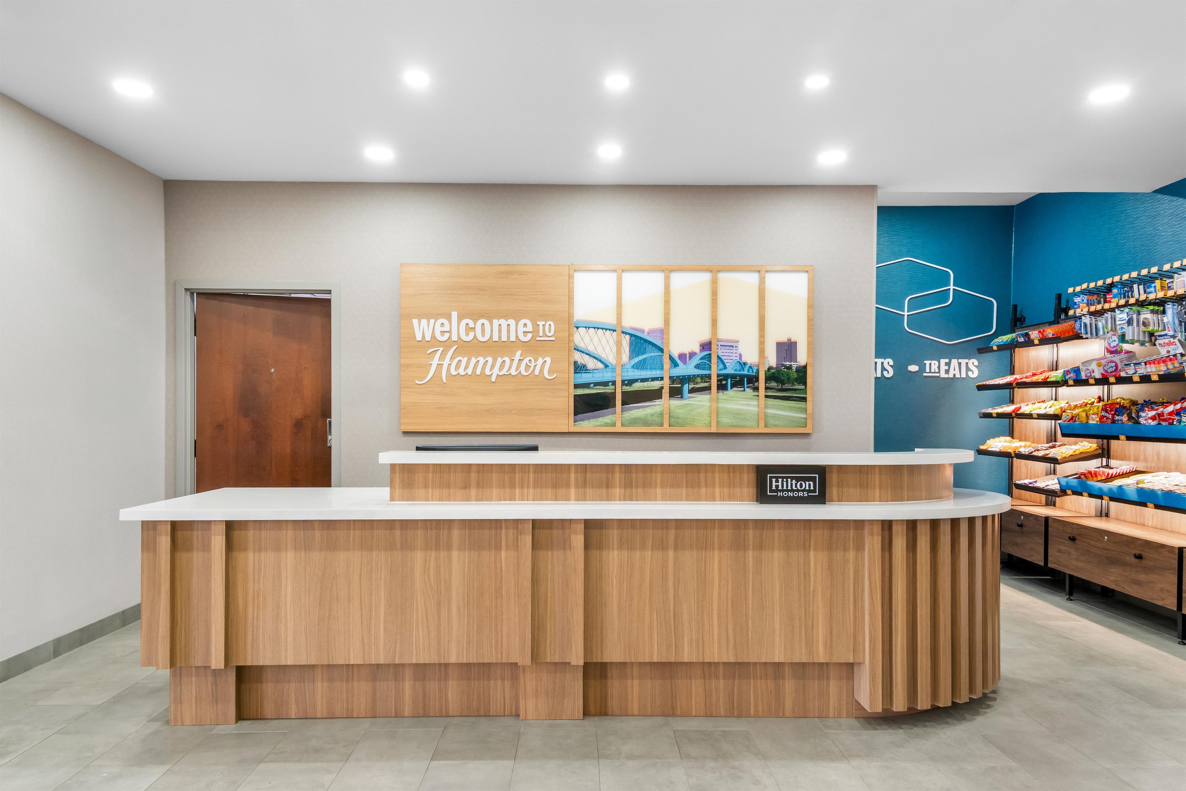 En receptionsdisk med en skylt som säger ”Välkommen till Hampton”, en väggmålning som föreställer stadens silhuett och en snackbar med ett varierat utbud av mat och dryck.