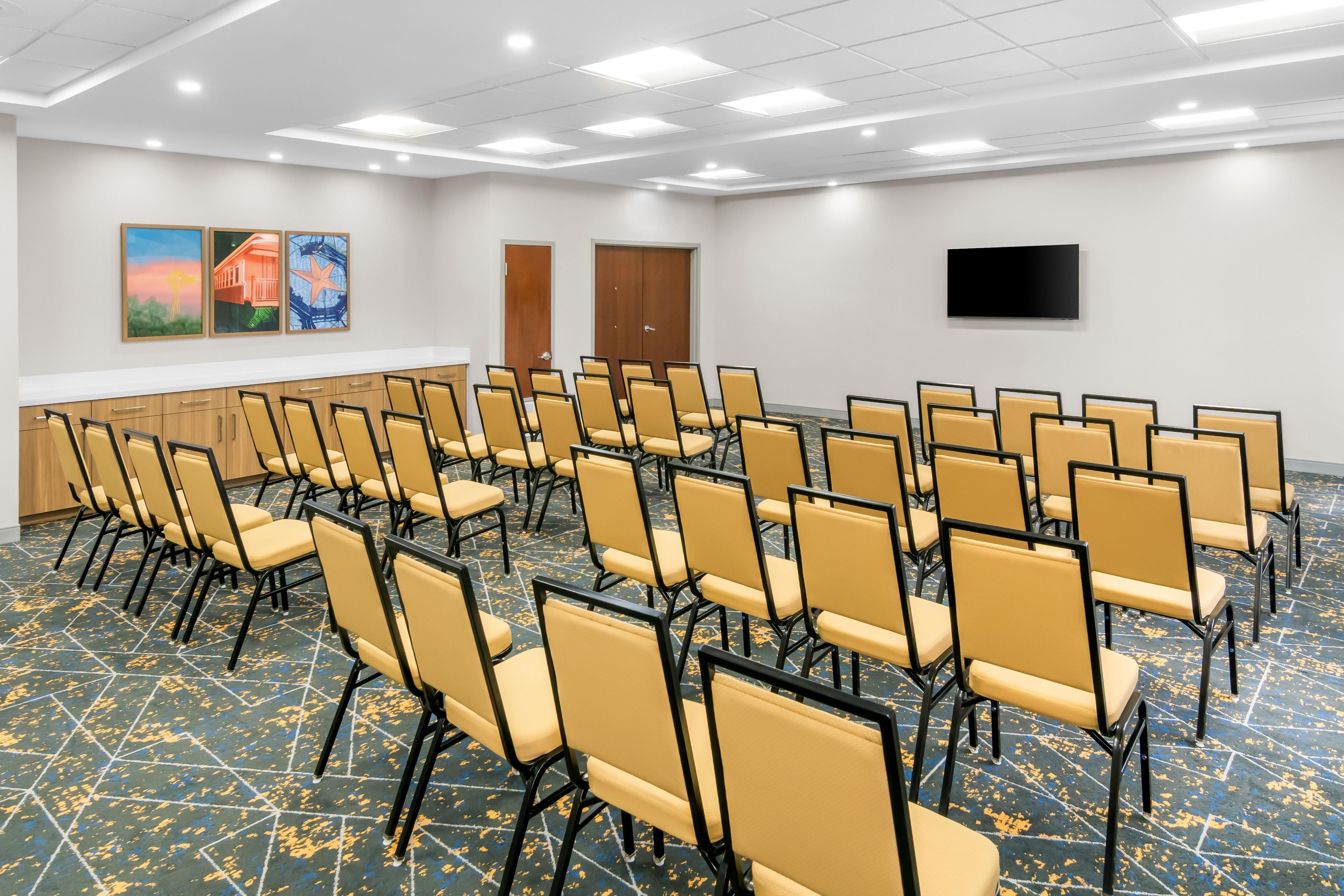 Un salón de conferencias con filas de sillas, una televisión de pantalla plana y obras de arte en las paredes.