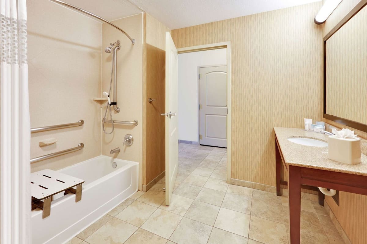 A bathroom with a bathtub, shower, and sink, equipped with grab bars and a hand dryer.
