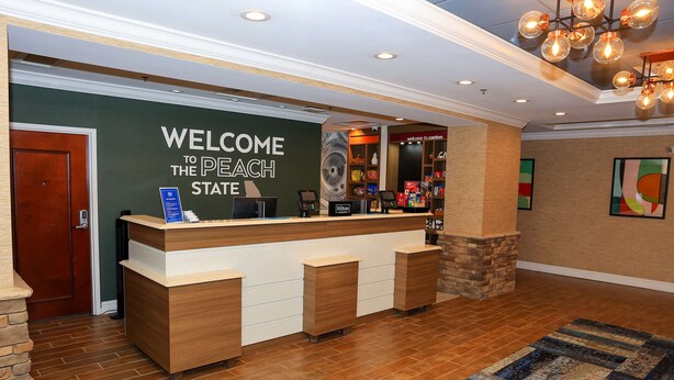 A reception desk with a "Welcome to the Peach State" sign, a digital kiosk, and a display of local attractions. - Hampton Inn Atlanta-Canton (Canton)
