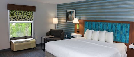 A hotel room with a large bed, a desk, a chair, a window with a view, and a wall with a blue and green pattern.