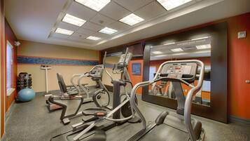 Een fitnessruimte met loopbanden, elliptische trainers en een spiegelwand.