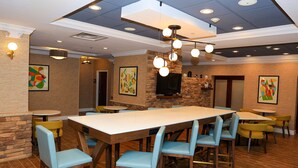 A restaurant with a long wooden table, blue chairs, and a stone accent wall. - Hampton Inn Atlanta-Canton (Canton)