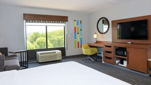 A hotel room with a bed, a desk, a chair, a TV, a heater, and a window with a view of trees. - Hampton Inn Atlanta-Canton (Canton)