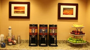 Una cocina de hotel con tres cafeteras, una presentación de frutas y dos cuadros en la pared.