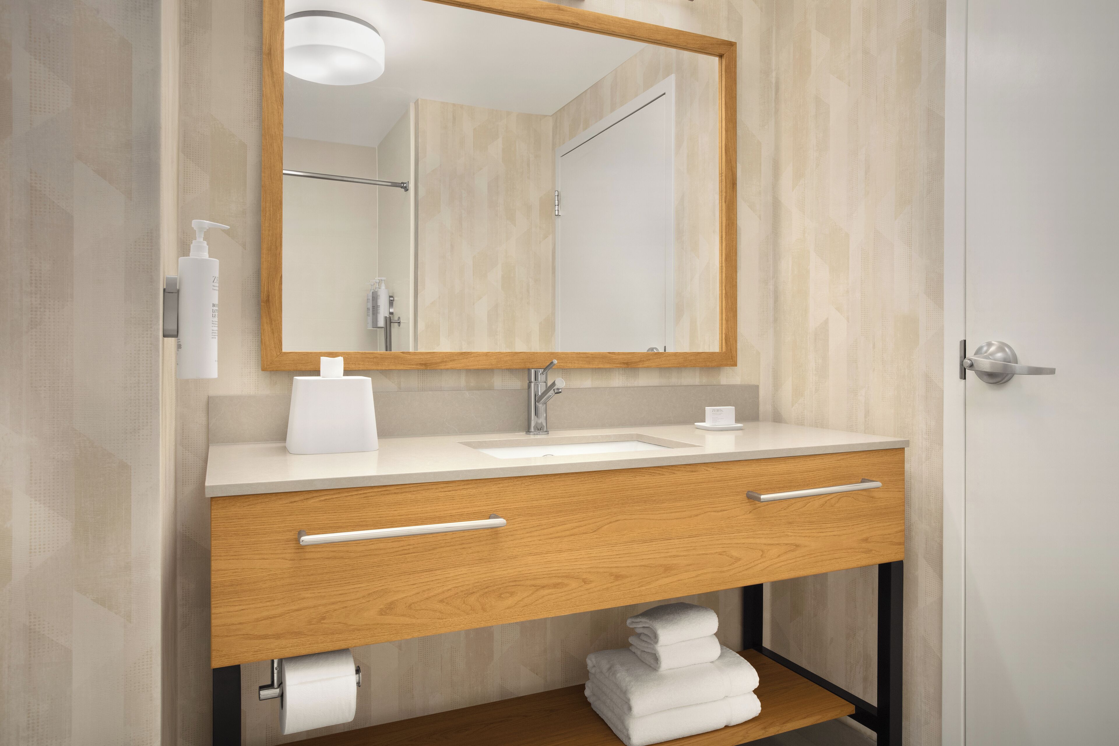 A modern bathroom with a wooden vanity, a large mirror, and a towel rack.