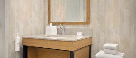 Un baño moderno con tocador de madera, un espejo grande y una pila de toallas blancas sobre una mesita.