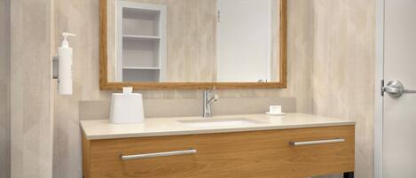 A bathroom with a wooden vanity, a white sink, a mirror, and a towel rack.