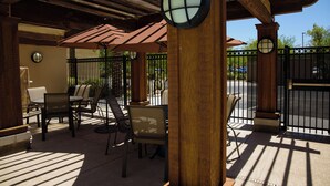 An outdoor patio area with wooden beams, a covered seating area with chairs and tables, and a gated entrance. - Hampton Inn & Suites Phoenix Chandler-Fashion Center AZ (Chandler)