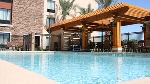 A pool area with a wooden pergola, lounge chairs, and a building with a brick facade and multiple windows. - Hampton Inn & Suites Phoenix Chandler-Fashion Center AZ (Chandler)
